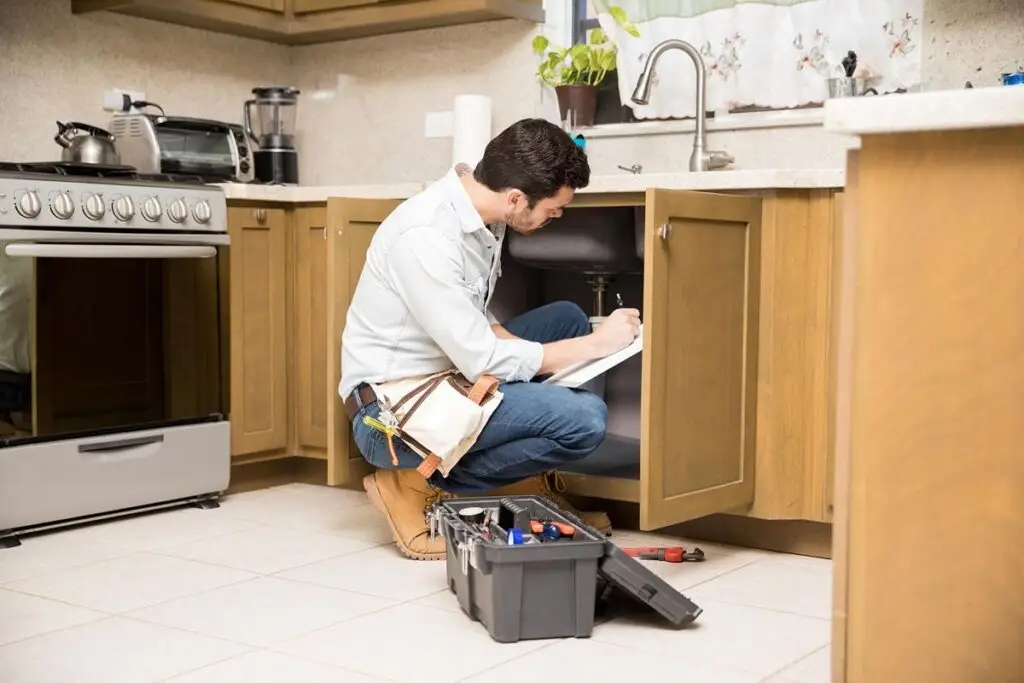 Licensed plumber working beneath a kitchen sink
